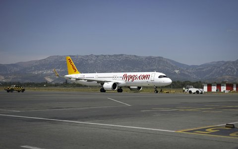 Ein weiß-gelbes Verkehrsflugzeug auf dem Rollfeld am Flughafen Tirana, dahinter graue Berge unter blauem Himmel