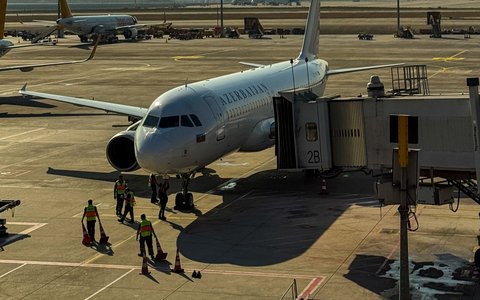 An airliner with Azerbaijan lettering at a jet bridge on the apron at Baku Airport, with ground crew beside it