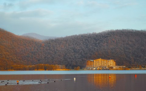 Nohur Lake with ducks on the water, a hotel on the far shore and wooded hills behind in autumn colour