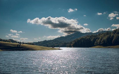 Breiter Fluss vor bewaldeten Hügeln am gegenüberliegenden Ufer bei Lənkəran unter blauem Himmel mit großen weißen Wolken