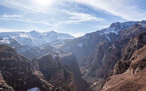 Snow-capped mountain ridges above a deep valley near Quba, under a blue sky with white clouds