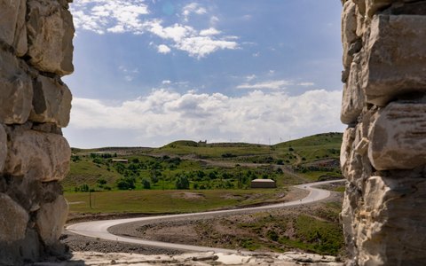 A winding road through green hills near Shamakhi seen between old stone walls, under a blue sky with white clouds