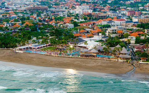Aerial view of the Canggu shore with waves on the sand, a beach club and the town spreading inland