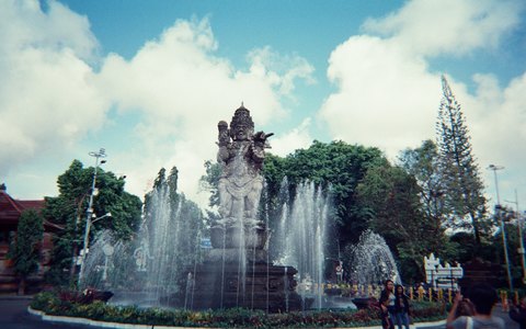 The Catur Muka statue and fountains at the centre of Denpasar, with trees and white clouds in a blue sky