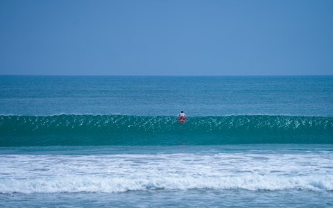 A lone surfer paddling out through turquoise waves at Kuta Beach under a clear sky