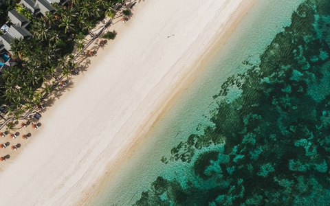 Weißer Sandstrand zwischen Palmen und klarem türkisfarbenem Wasser in Nusa Dua aus der Luft