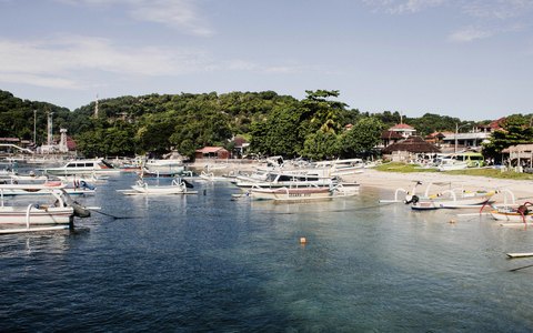 Outrigger boats moored in Padangbai harbour below green hills, under a blue sky with clouds