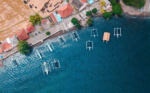 Draufsicht auf Auslegerboote, die in Buleleng vor einem Uferabschnitt mit roten Dächern und einer befestigten Promenade festgemacht sind