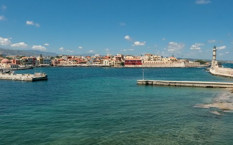 The Venetian harbour of Chania with old waterfront houses, the lighthouse on the breakwater and turquoise water under a blue sky