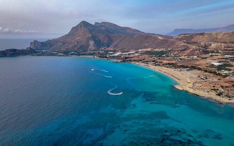 Aerial view of a long sandy beach curving round a turquoise bay below a mountain headland