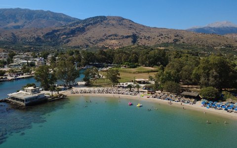 Aerial view of a sandy beach and turquoise water at Georgioupoli, with green trees and mountains behind