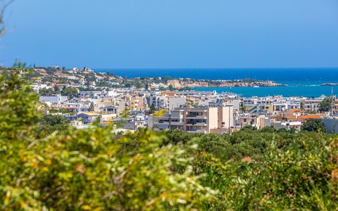 The white buildings of Heraklion spread down to a blue sea, with green shrubs in front and a clear blue sky
