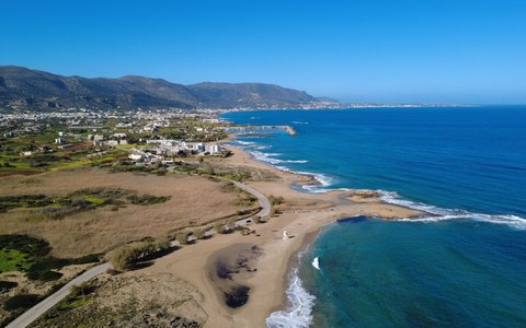 Aerial view of a sandy shore and turquoise shallows at Malia, with low mountains along the coast