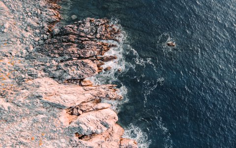 Aerial view of pinkish rocks meeting deep blue sea on the coast at Plakias
