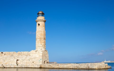 A stone lighthouse at the end of the harbour wall in Rethymno against a vivid blue sky