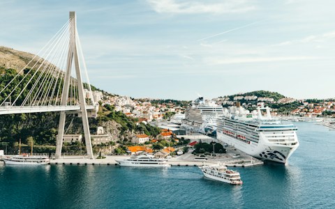 Cruise ships and small passenger boats at the Gruž port in Dubrovnik, under a white cable-stayed bridge and hillside houses