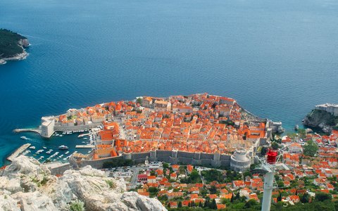 Aerial view of Dubrovnik's walled old town and red roofs on a rocky headland above a deep blue sea