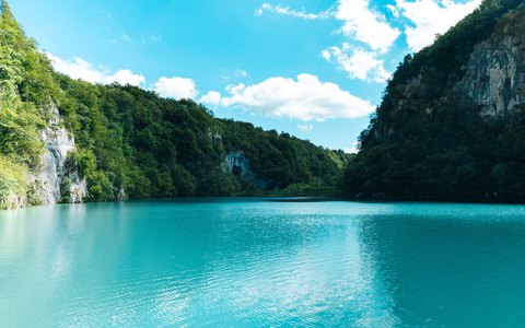 A turquoise lake between steep forested cliffs, with white clouds in a blue sky