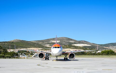 An orange and white airliner on the apron at Split Airport, with green hills behind under a blue sky
