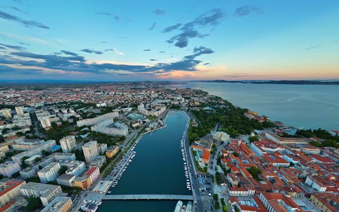 Aerial view of Zadar's peninsula, harbour and rooftops beside the sea under a sunset sky