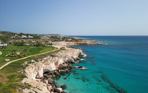 Aerial view of pale rocky sea cliffs with a footpath along the top, above clear turquoise water