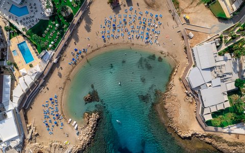 Aerial view of a small sandy cove with sun loungers around clear turquoise water