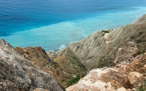 Pale rocky cliffs dropping into a bright turquoise sea under a blue sky