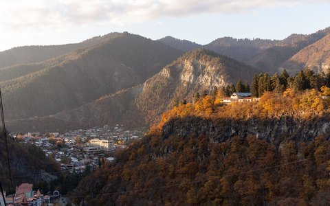 A forested mountain valley in autumn colours with a town in the valley floor, in warm sunlight