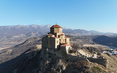 Aerial view of the stone Jvari Monastery on its hilltop with mountains beyond