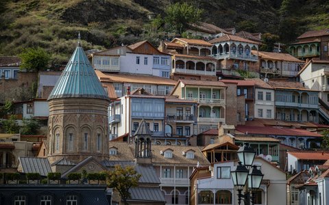 Alte Häuser mit Holzbalkonen und Kirche mit grünem Kegeldach am Hang in der Altstadt von Tiflis