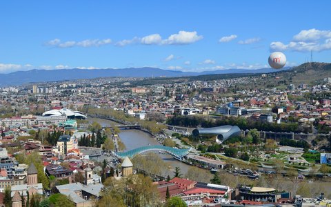 Aerial view of Tbilisi along the Mtkvari river with the Bridge of Peace, under a clear blue sky