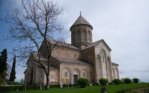 A large stone Orthodox church with a domed tower beside a bare tree in Telavi, under a pale sky