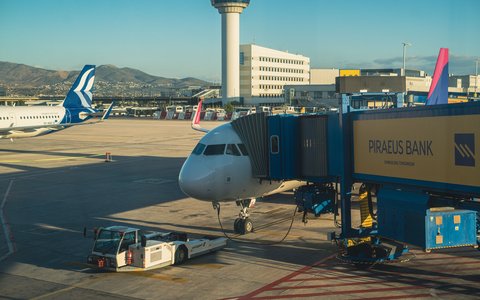 Verkehrsflugzeug an einer Fluggastbrücke auf dem Vorfeld des internationalen Flughafens Athen, dahinter der Kontrollturm