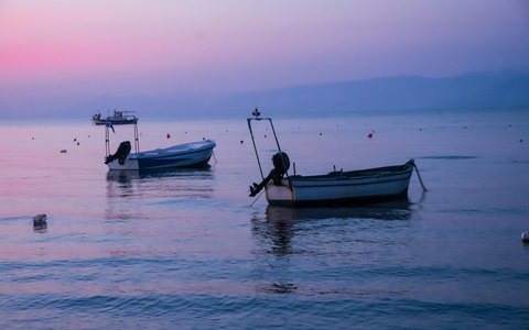 Small boats on calm water off Kavos beach under a pink evening sky