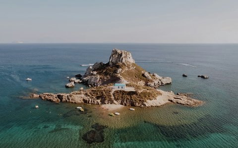 Kleine Felseninsel mit einem kleinen weißen Gebäude im klaren türkisfarbenen Meer vor Kos