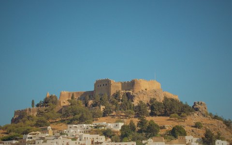 The walls of the Lindos acropolis on a rocky hilltop above white houses, under a blue sky