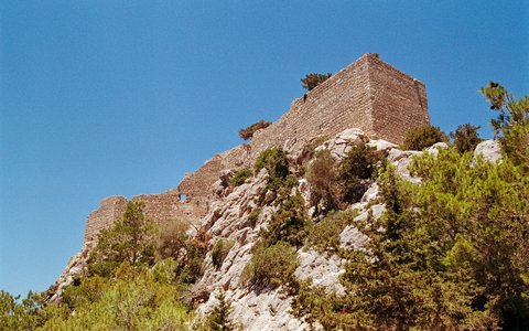 Stone walls of Monolithos castle on top of a rocky outcrop under a blue sky
