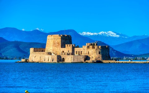 The small stone Bourtzi fortress on its islet in deep blue water, with mountains behind under a blue sky