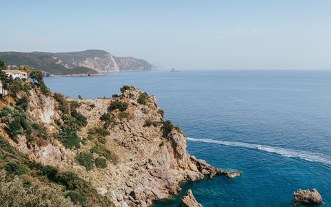 A green headland above turquoise water on the Corfu coast, seen from the monastery hill under a clear sky