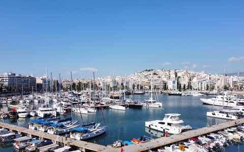 Rows of boats in Marina Zeas with the white buildings of Piraeus behind, under a clear blue sky