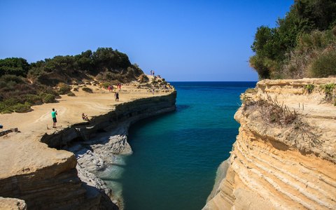 Pale sandstone cliffs either side of a narrow inlet of turquoise water at Sidari, under a deep blue sky