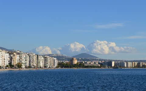 The Thessaloniki seafront with the White Tower and apartment blocks across blue water, and mountains with white clouds behind