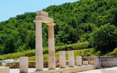 Restored stone columns of the ancient palace at Vergina in front of green wooded hills, under a blue sky