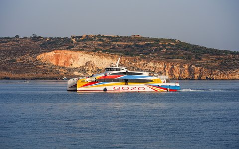 A brightly painted Gozo ferry crossing the blue channel past pale limestone cliffs
