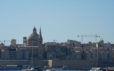 Boats in the harbour in front of Valletta's domes and church towers, under a clear blue sky
