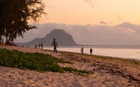 Flic en Flac beach at sunset with trees on the sand, a few walkers and Le Morne Brabant on the horizon