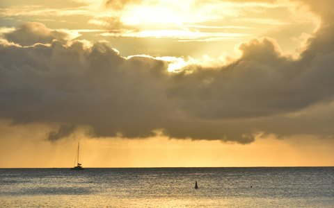 Golden evening light breaking through heavy clouds over a calm sea at Pereybere