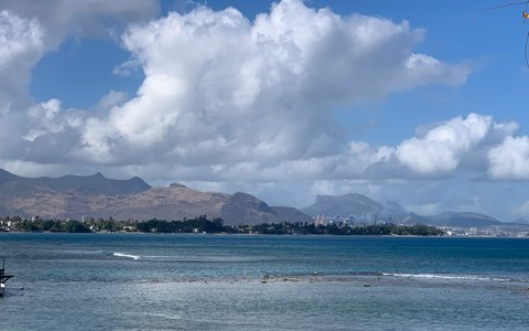The sea at Port Louis with the town and its mountains behind, under a blue sky full of white clouds