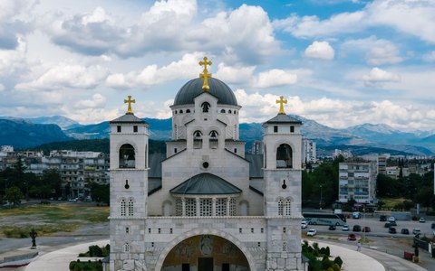 A large stone Orthodox cathedral with golden crosses on its domes, under a blue sky with white clouds