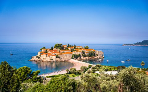 The walled islet of Sveti Stefan with red roofs, joined to the shore by a sand causeway, in a deep blue sea